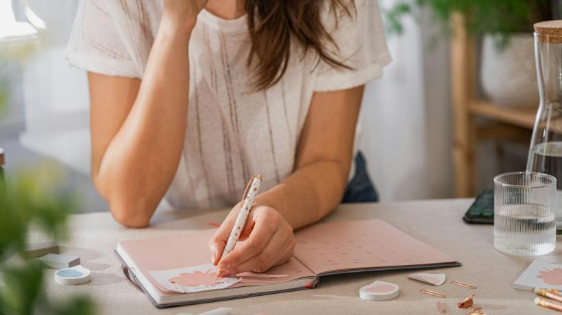 Eine Frau sitzt an einem Tisch und schreibt in ein Journal.