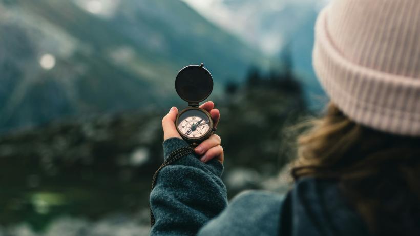 Eine Frau hält einen Kompass vor sich, im Hintergrund ist eine Berglandschaft