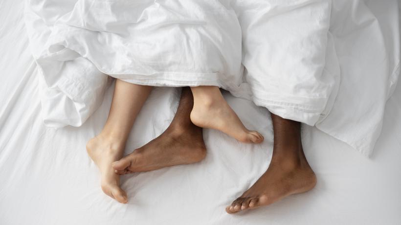 Foto: freepik.com Man sieht die nackten Füße zweier Menschen unter einer weißen Decke herausragen.