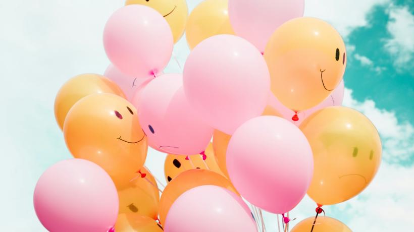 Ein Bündel rosa und orangener Luftballons, auf die lächelnde Smileys gemalt sind