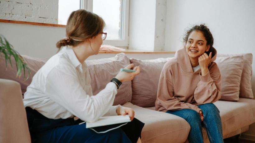 Foto: Polina Zimmermann – pexels.com Zwei Frauen unterhalten sich freundlich auf einer Coach, die eine hat einen Schreibblock auf dem Schoß