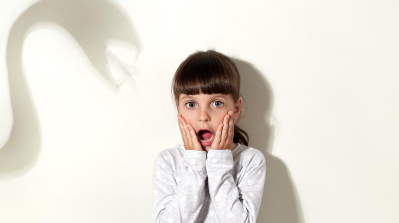 Foto: user18526052 – freepik.com Ein kleines Mädchen schaut erschrocken in die Kamera, neben ihr ist ein schlangenartiger Schatten an der Wand.