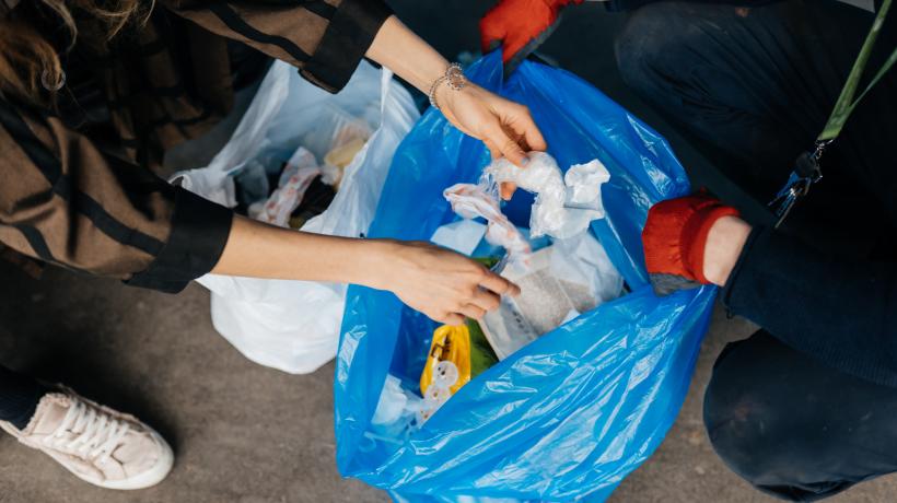 Foto: teksomolika – freepik.com Zwei Menschen füllen einen Müllbeutel mit Krams.