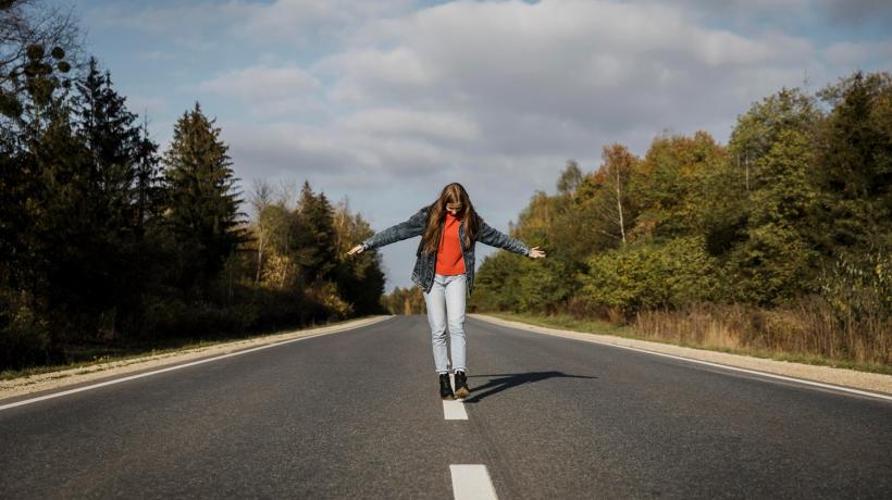 Foto: freepik.com Eine Frau balanciert auf dem Mittelstreifen einer breiten Landstraße