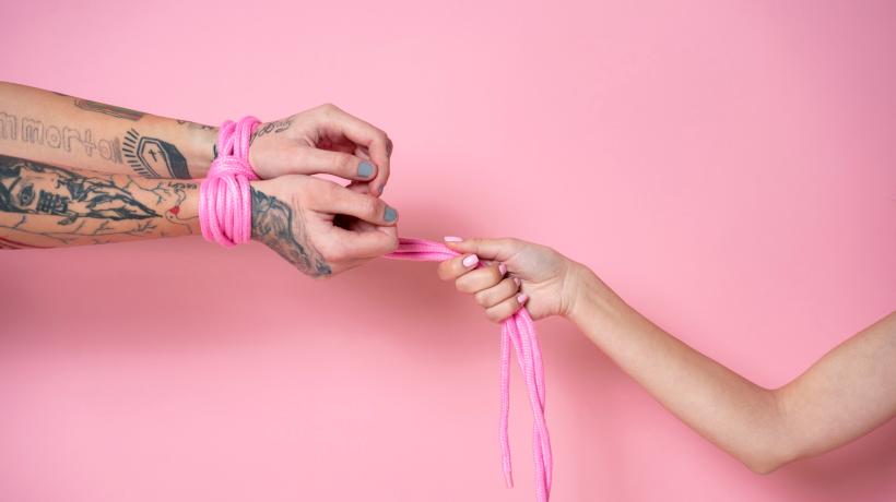 Foto: freepik.com Vor einem rosa Hintergrund sieht man eine Hand, die ein rosa Band hält, mit dem die Hände ihres Gegenübers zusammengebunden sind