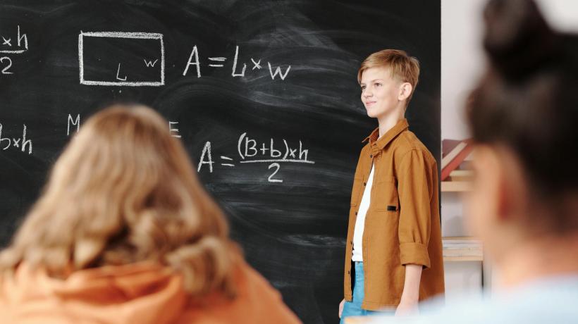 Foto: Max Fischer – pexels.com Ein Kind steht an der Tafel und rechnet vor, Mitschülerinnen sehen zu.