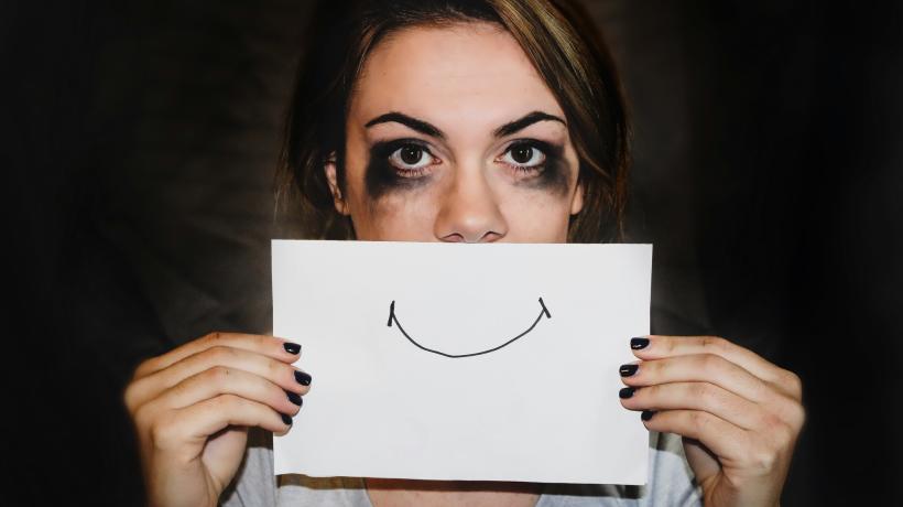 Foto: Sydney Simsa – unsplash.com Eine Frau mit verlaufener Schminke hält sich ein Blatt Papier vor das Gesicht, auf dem Papier ist ein lächelnder Mund gezeichnet