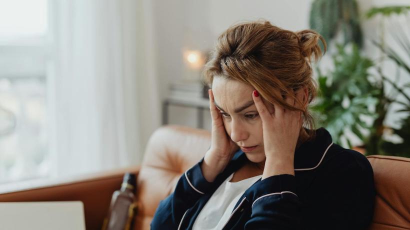 Foto: kaboompics – pexels.com Eine Frau sitzt auf einem Sofa und fasst sich müde an die Schläfen.