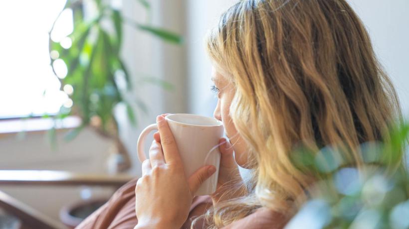 Foto: Kevin Malik – pexels.com Eine Frau schaut aus dem Fenster, während sie in eine Decke gehüllt ist und Tee trinkt.