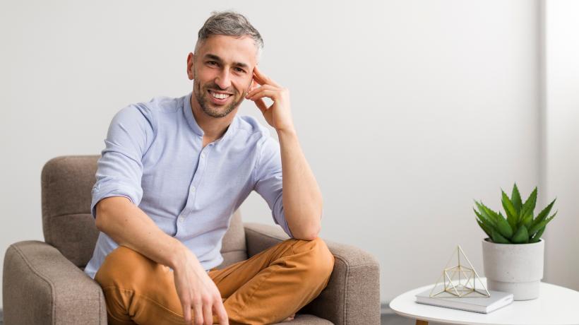Foto: freepik.com Ein Mann sitzt im Schneidersitz in einem Sessel und lächelt offen in die Kamera.