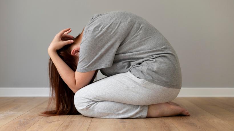 Foto: freepik.com Eine Frau kniet am Boden und hat sich wie ein Igel eingerollt.