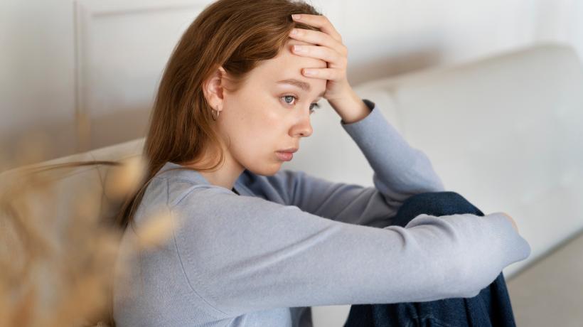Foto: freepik.com Junge Frau sitzt auf einem Sofa und schaut traurig.