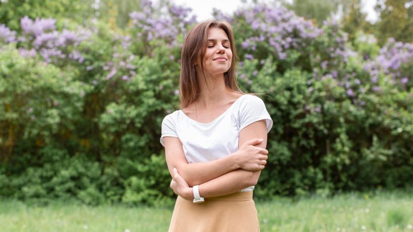 Foto: freepik.com Eine Frau umarmt sich selbst und steht lächelnd auf einer Wiese.