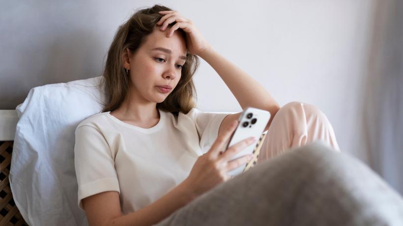 Eine junge Frau schaut sitzend auf ihr Smartphone