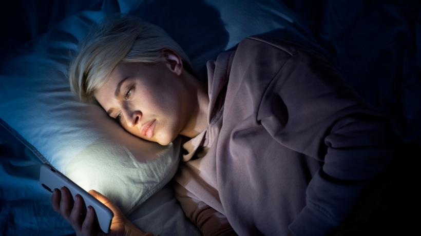 Ein Jugendlicher liegt im Dunkeln im Bett und schaut auf sein Smartphone.