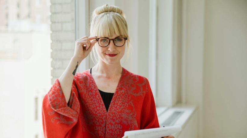 Foto: RDNE Stock project – pexels.com Eine blonde Frau mit Brille fasst sich an die Brille, sie hält einen Papierblock in der Hand.