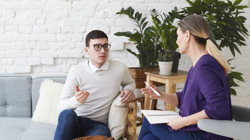 Foto: shurkin_son – freepik.com Ein Mann und eine Frau sitzen sich schräg gegenüber in einem hellen Raum mit Sofas und Pflanzen.