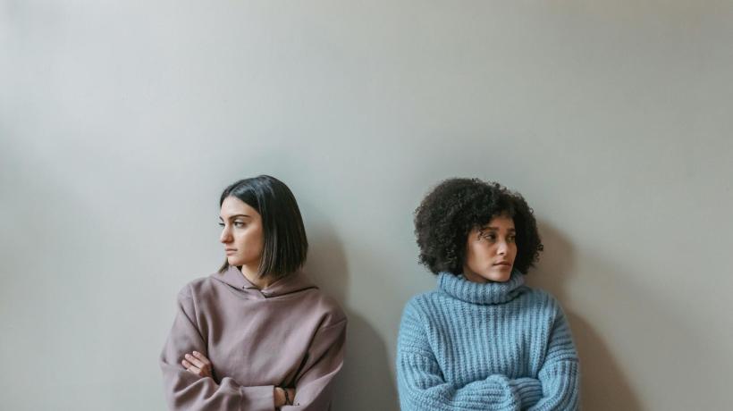 Zwei Frauen sitzen einander abgewandt nebeneinander an einer hellen Wand.