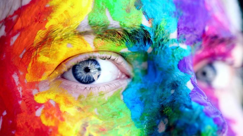 Nahaufnahme eines regenbogenfarben angemalten Gesichts einer Person mit blauen Augen.
