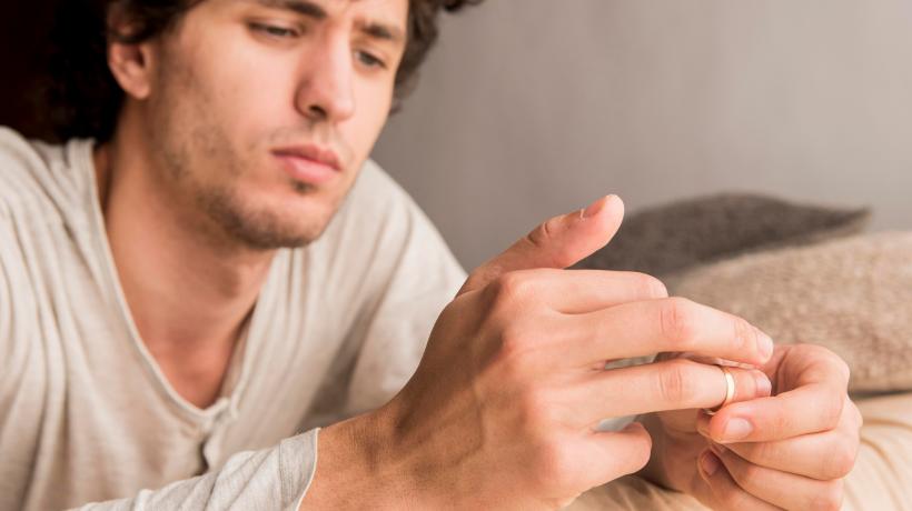 Foto: Freepik.com Ein Mann sitzt nachdenklich auf einem Sofa und zieht sich den Ring vom Finger