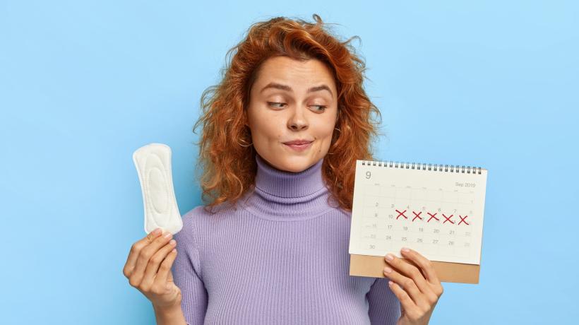 Eine Frau hält eine Binde und einen Zykluskalender in der Hand und schaut skeptisch.