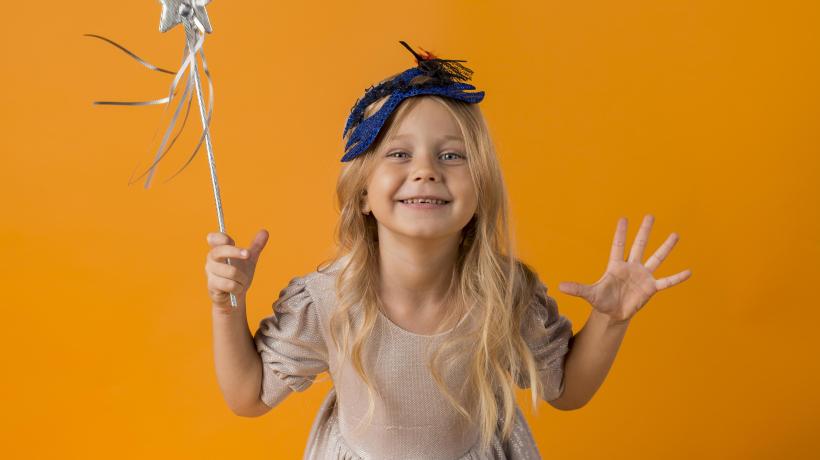 Foto: freepik.com Ein kleines Mädchen mit Zauberkostüm vor orangenem Hintergrund