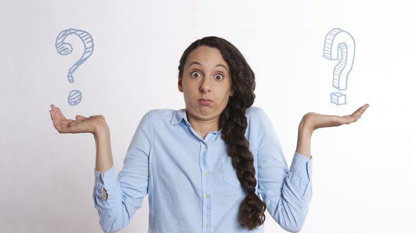 Eine Frau zieht die Schultern hoch und hebt die Hände, über deren Flächen je ein Fragezeichen schwebt