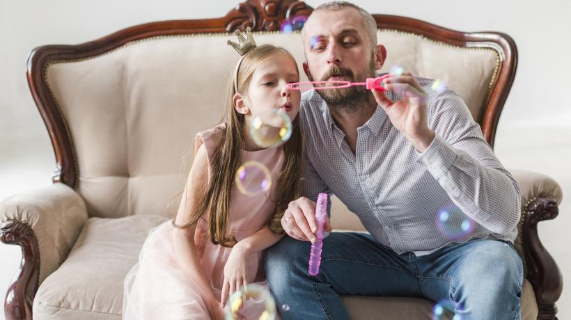 Foto: freepik.com Ein Mann und ein Mädchen sitzen auf einem Sofa und pusten Seifenblasen.