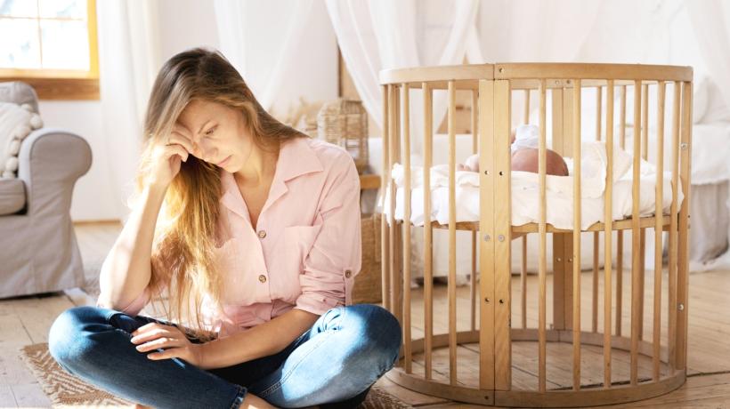 Eine junge Mutter hockt neben dem Kinderbett und liest.