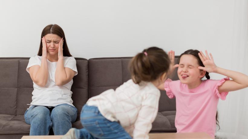 Zwei Kinder albern rum, ihre Mutter sitzt auf dem Sofa und hält sich die Ohren zu.