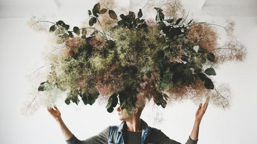 Eine Person, über und auf deren Gesicht ein Pflanzenwirrwarr schwebt