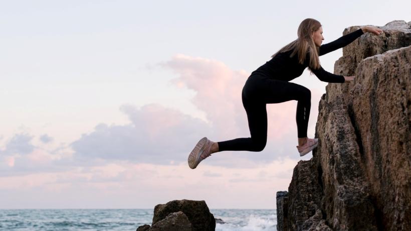 Eine Frau klettert einen Felsen am Meer hoch.