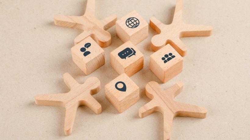 Vier Holzmännchen und fünf Würfel mit Symbolen liegen auf einer Holzoberfläche.