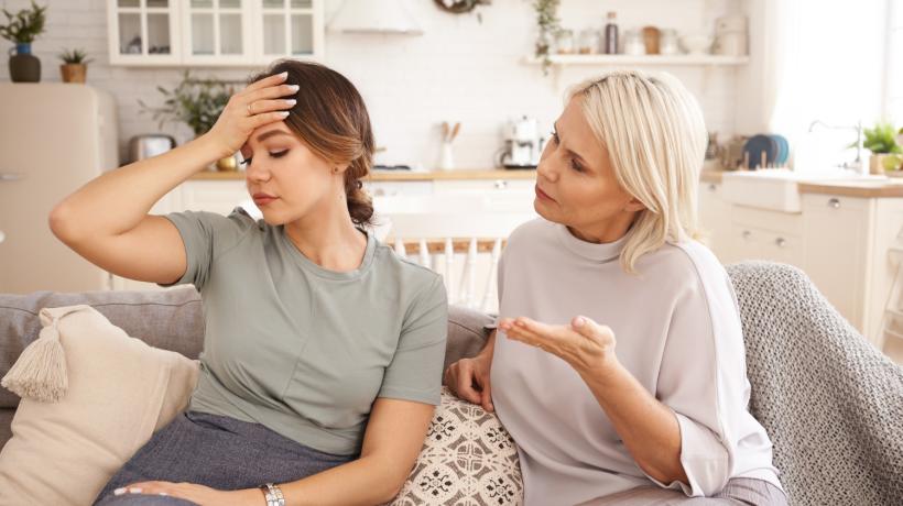 Eine junge und eine mittelalte Frau sitzen nebeneinander auf einem Sofa und unterhalten sich angestrengt.