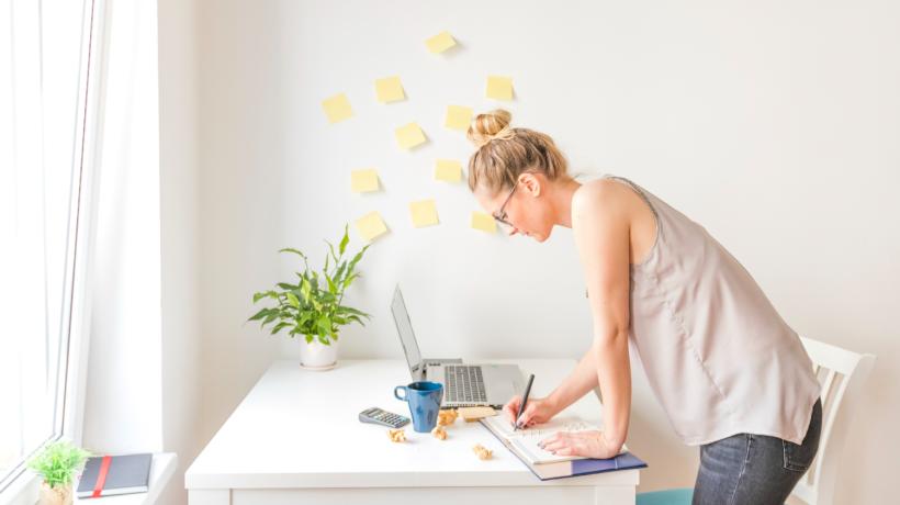 Eine blonde Frau beugt sich über Ihre Arbeitsmaterialien am Bürotisch.