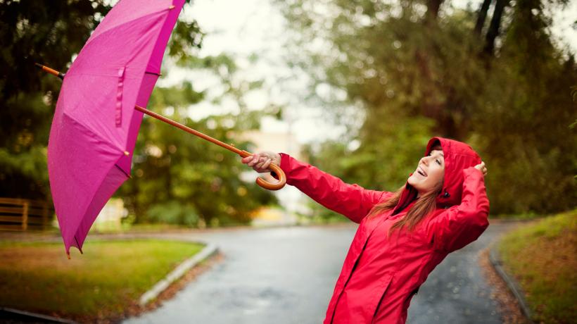 Eine Frau hält einen lila Regenschirm, der ihr fast weggeweht wird.