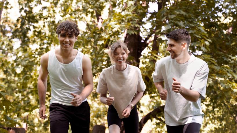 Drei junge Erwachsene in weißen T-Shirts joggen fröhlich durch den Wald.