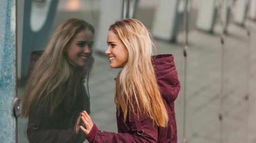 Eine blonde junge Frau spiegelt sich in einer Glaswand.