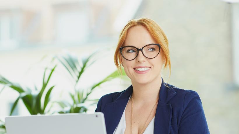 Eine junge Frau sitzt lächelnd an einem weißen Laptop.