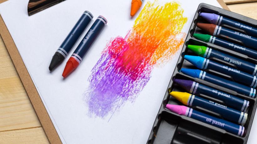 Eine Packung Wachsmalstifte. Mit ein paar Farben wurde auf ein weißes Papier gemalt.