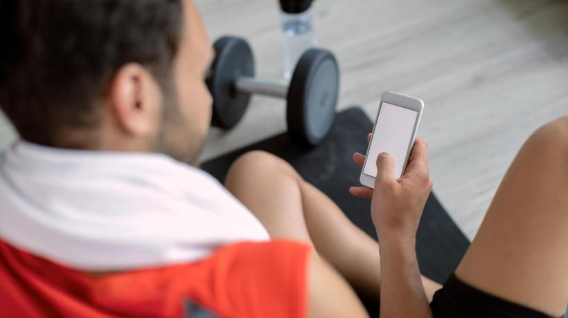 Ein junger Mann mit Smartphone im Fitnessstudio.