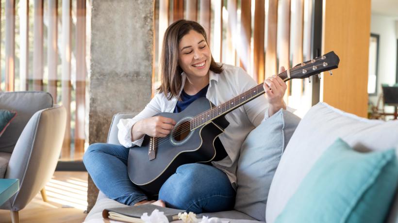 Eine Frau spielt Gitarre, auf einem Sofa sitzend.
