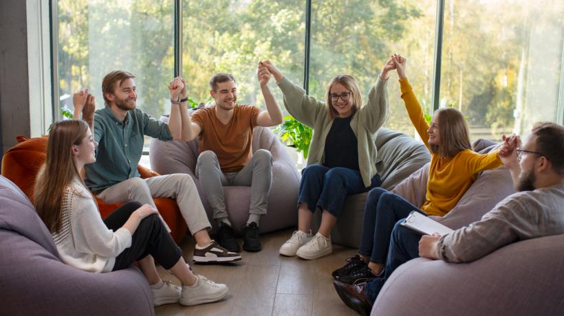 Ein Sitzkreis aus Menschen, die sich teils an der Hand halten.