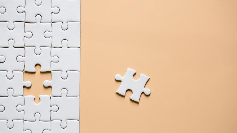 Ein weißes Puzzle auf orangenem Grund, bei dem ein Puzzleteil fehlt