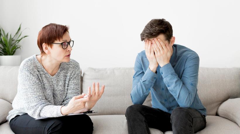 Eine Frau und ein Mann auf einem Sofa, er hält sich die Hände vor das Gesicht