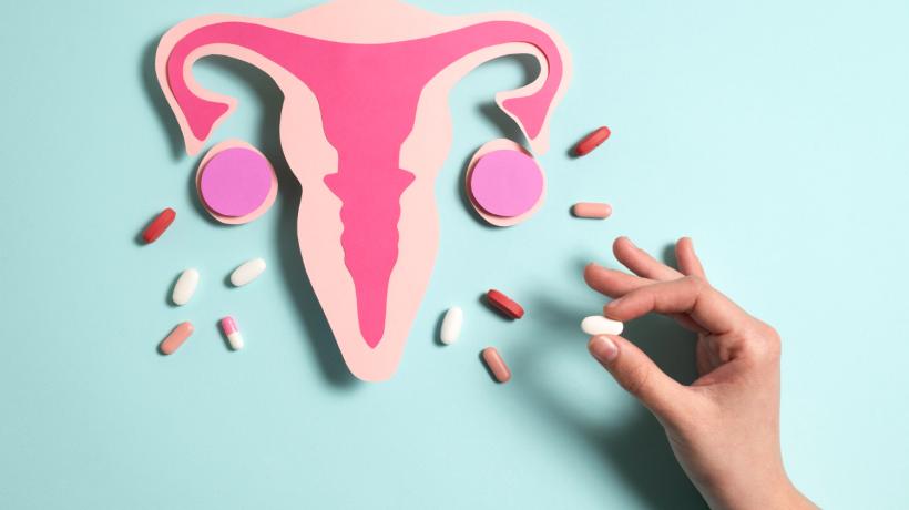 Illustration einer Gebärmutter mit Eierstöcken und Vagina. Drum herum verschiedene Pillen.