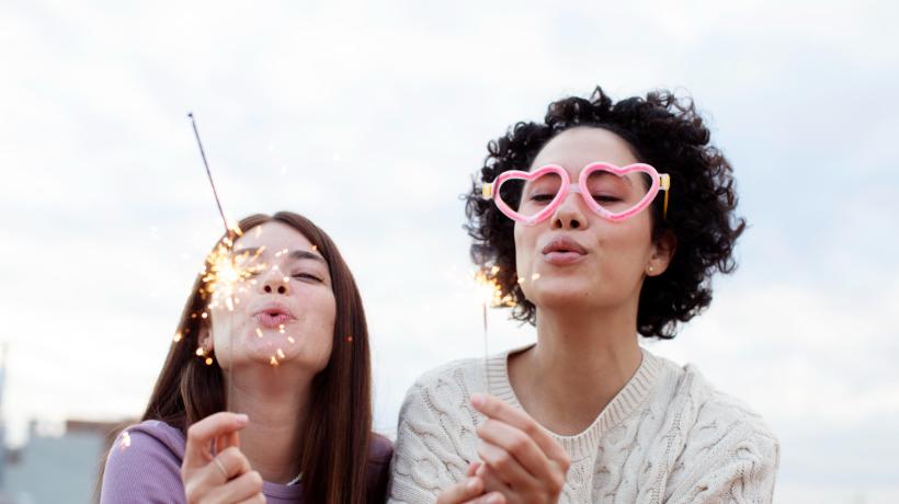 Zwei Frauen, eine mit Herzbrille, die andere mit einer Wunderkerze