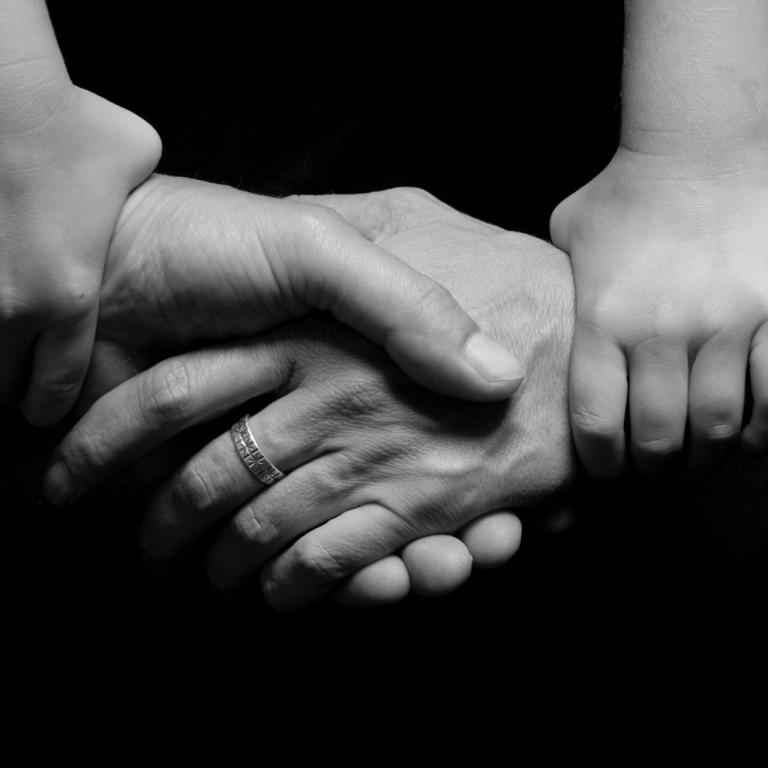 Elternhände, die einander halten und Kinderhände, die die Handgelenke der Eltern umfassen.