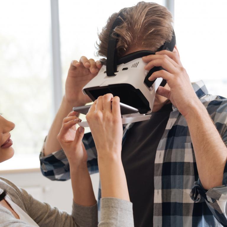Eine Frau hilft einem Mann, eine VR-Brille aufzusetzen.