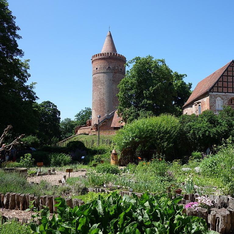 Burgturm mir Fachwerkhaus rechts daneben und Garten vor den Gebäuden